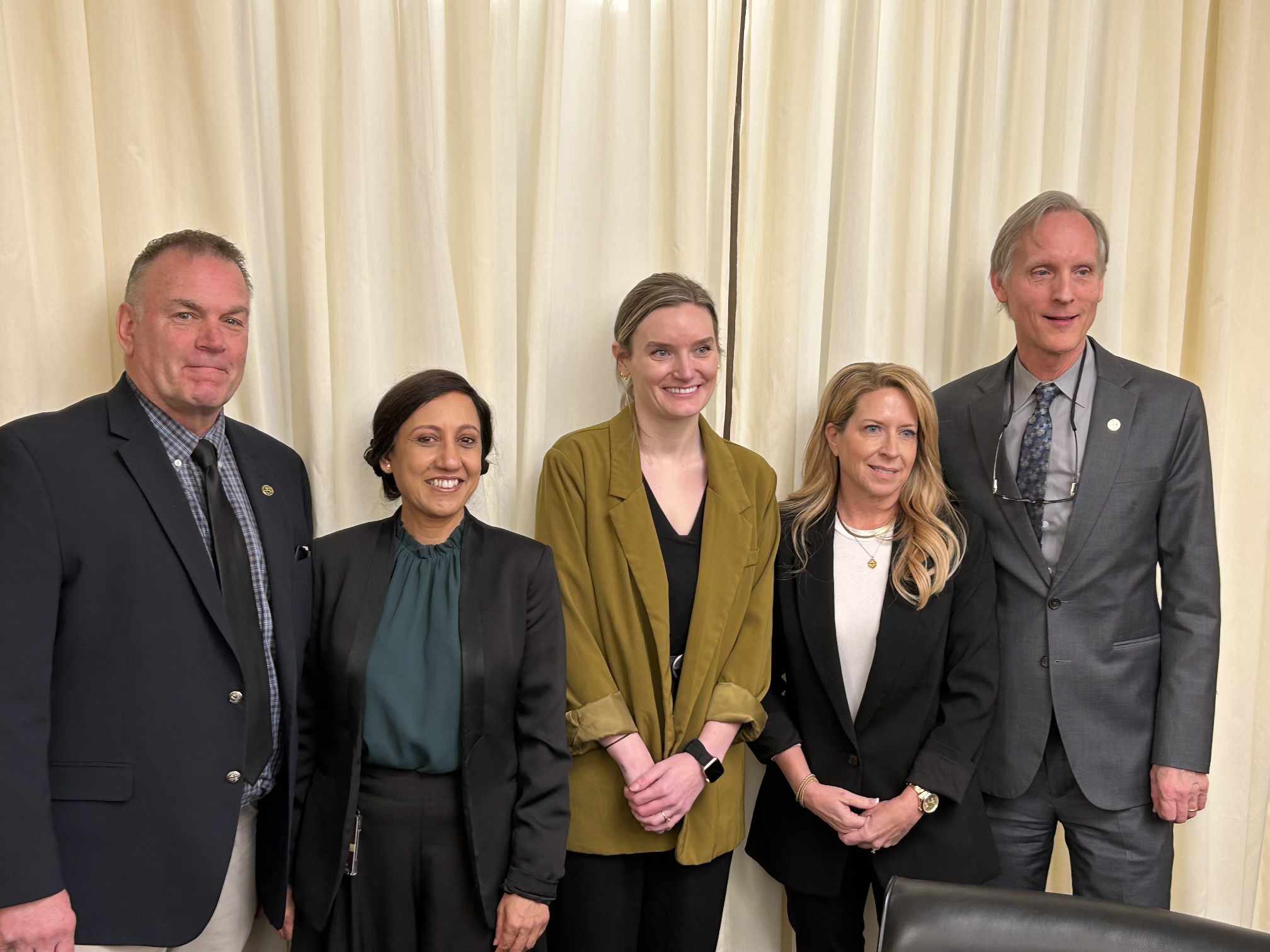 Rep. Dave Baker, Roli Dwivedi, MD, FAAFP, two other testifiers, and Rep. Robert Bierman, pictured standing in a line, at a committee hearing.